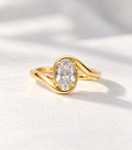 The Embrace, 2ct oval lab grown diamond bezel set engagement ring with bypass band in 9k yellow gold